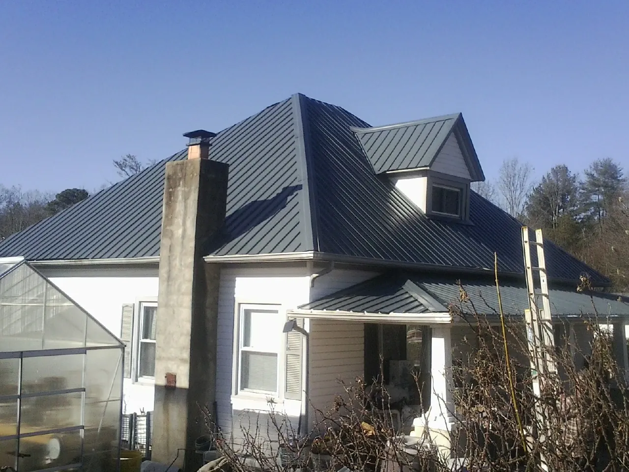 Dark blue standing seam metal roof on a white farmhouse with dormer — Slate & Tile Roof Repair by Roofing Brothers in Hickory Corners