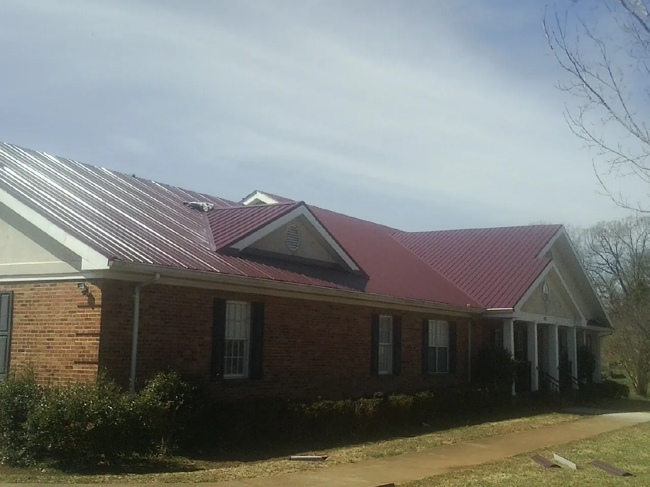 Red metal roof with gabled entries on a long brick building, from a Hail Damage Roof Repair job in Hickory Corners
