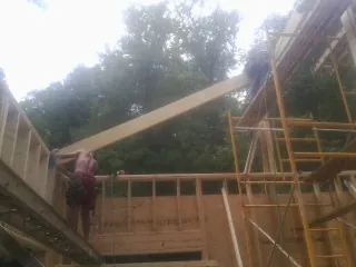 Carpenter raising a rafter beam on a new second story frame in Hickory Corners