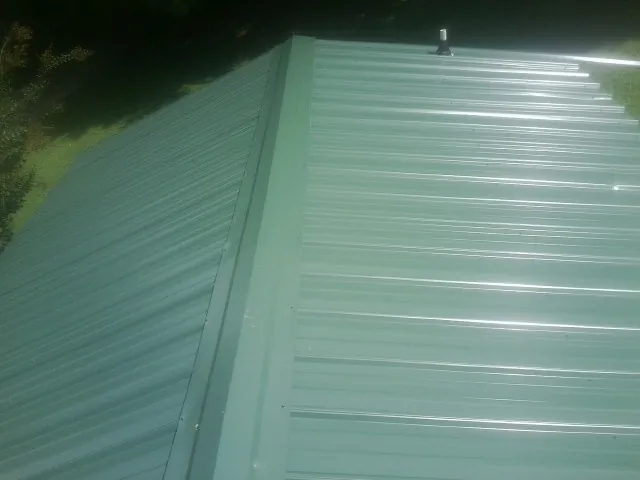 New green metal panels meeting at the ridge of a roof — Flat Roof Repair work by our crew in Hickory Corners