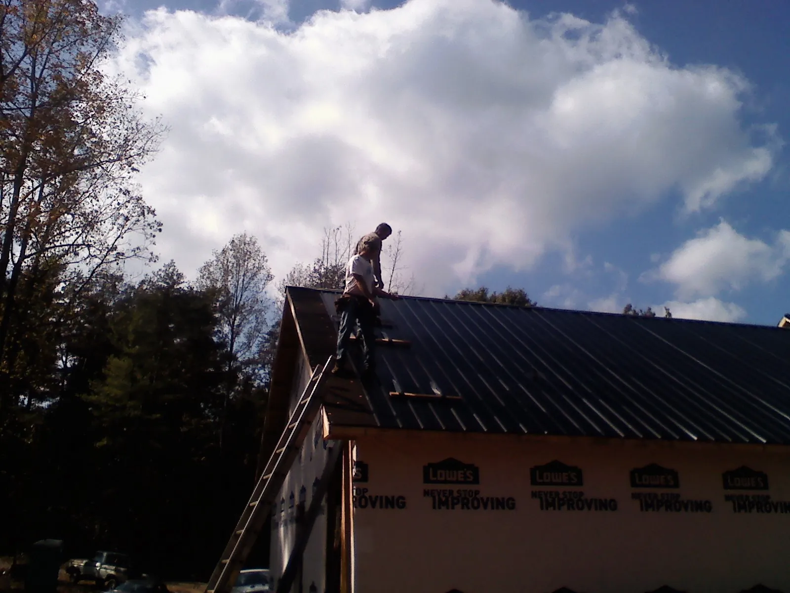 Roofer fastening dark metal panels high against a cloudy sky, from a Roof Inspection job in Hickory Corners
