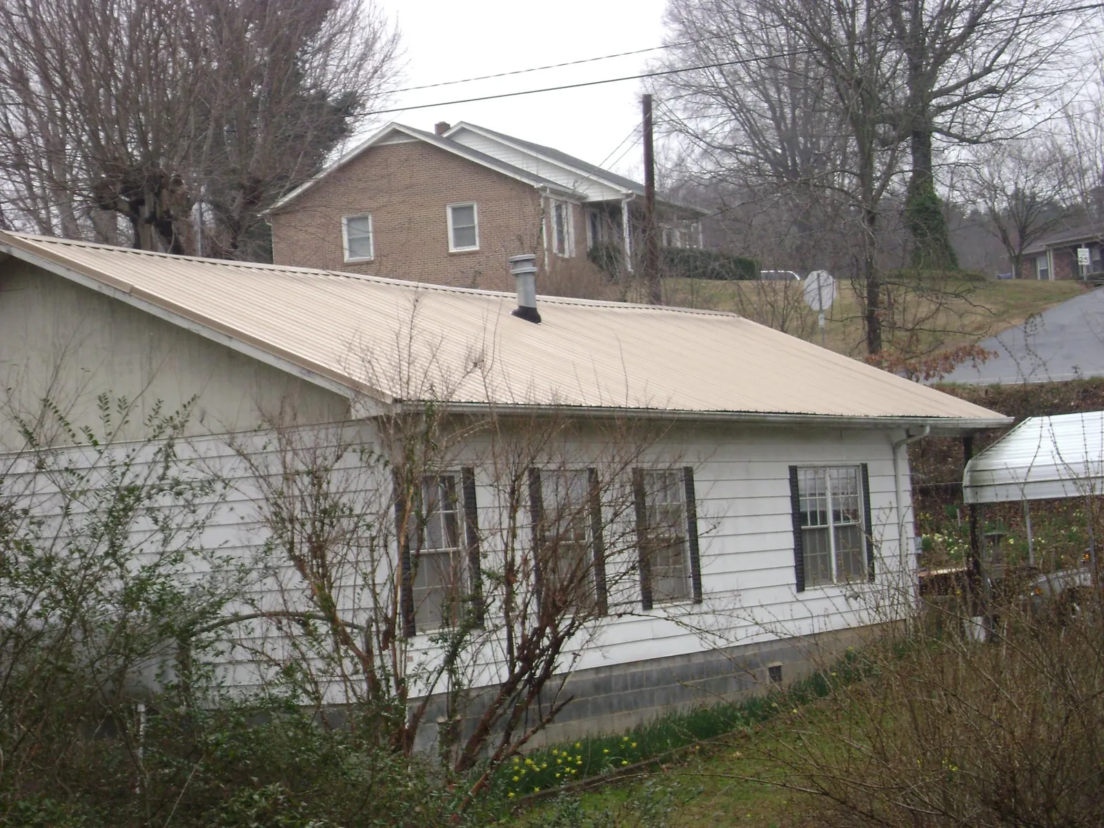 Tan metal roof on a white sided house set into a hillside — Commercial Roofing by Roofing Brothers in Hickory Corners