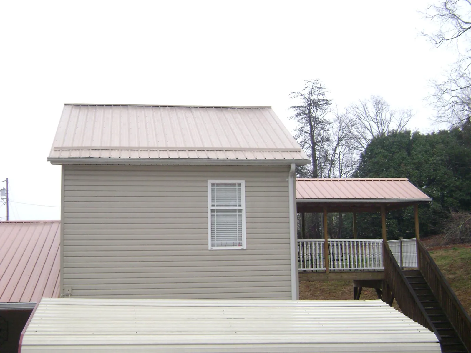 Tan metal roofs on a two story addition and attached porch, from a Roof Replacement job in Hickory Corners